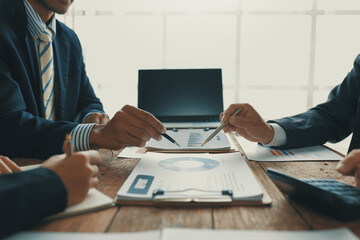 Business team analyzing financial data using laptop and calculator, pointing at charts and graphs,...