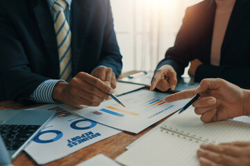 Business people meeting in an office, collaborating on laptops while analyzing financial documents...