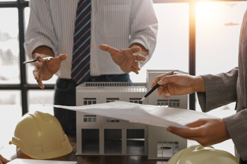 Architects and engineers engaged in a collaborative meeting, analyzing detailed blueprints and examining a scale model of a building, focused on planning the construction project