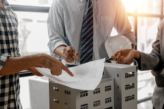 Architects and engineers engaged in a discussion, pointing at a detailed building model and blueprint during a collaborative meeting focused on project planning and design strategies