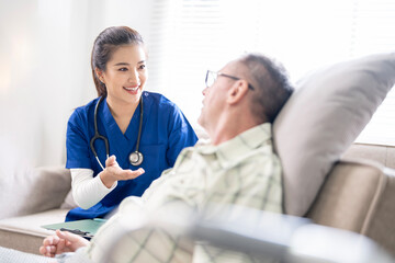 Fototapeta premium Young friendly asian female nurse or caregiver talking to elderly man in nursing home