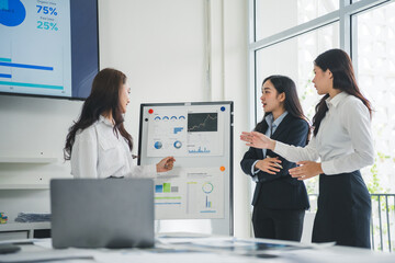 Businesswomen analyzing financial statistics displayed on whiteboard and discussing marketing...