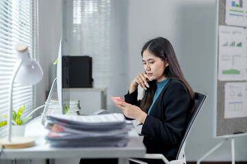 Young businesswoman using smartphone in bright modern office with desktop computer and paperwork,...