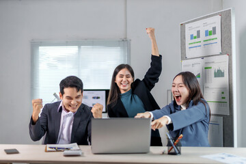 Euphoric businesspeople are celebrating a successful project while looking at a laptop in the...