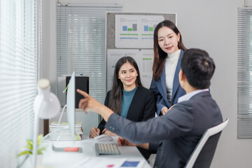 Three asian businesspeople are discussing work, a businessman is pointing at a desktop computer...