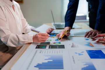 Business team analyzing financial data and pointing at charts and graphs with pens while discussing...