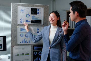 Two Asian businesspeople engaging in discussion and analyzing charts and graphs that illustrate...