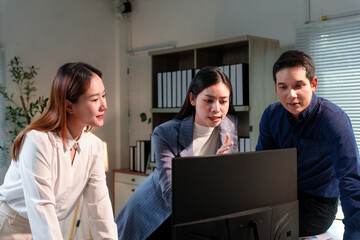 Three asian businesspeople are discussing work while looking at a desktop computer in the office,...