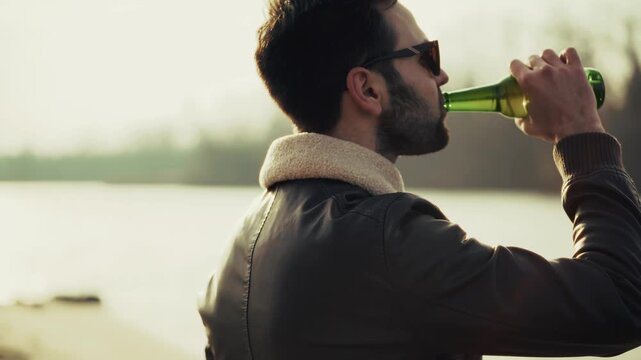 Stylish man with sunglasses savoring drink from green bottle