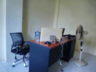 Abstract blurred empty office interior with a desk, chair, monitor, and fan. Ideal for general backgrounds, conceptual designs, or conveying a quiet workspace ambiance.