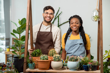 Young man and woman selling cactuses in a flower shop and looking happy