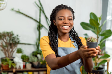 Young cute african american woman holding a pot with cactus and smiling