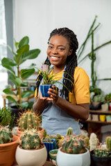 Young cute african american woman holding a pot with cactus and smiling