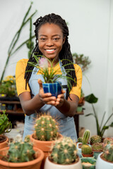 Young cute african american woman holding a pot with cactus and smiling