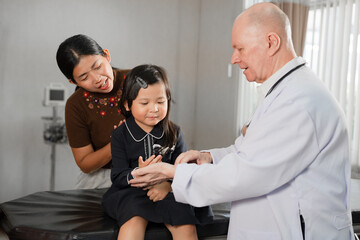 Caucasian Doctor check Asia kid girl patience's pulse by fingers with assistant at hospital