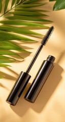 Black mascara tube and wand with a palm leaf casting shadows on a tan background