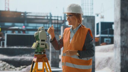 Female surveyor using theodolite giving thumbs up at construction site