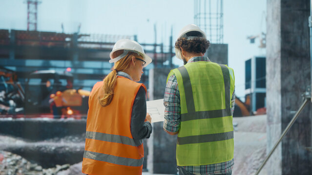 Engineers discussing blueprint at construction site with excavator working in background