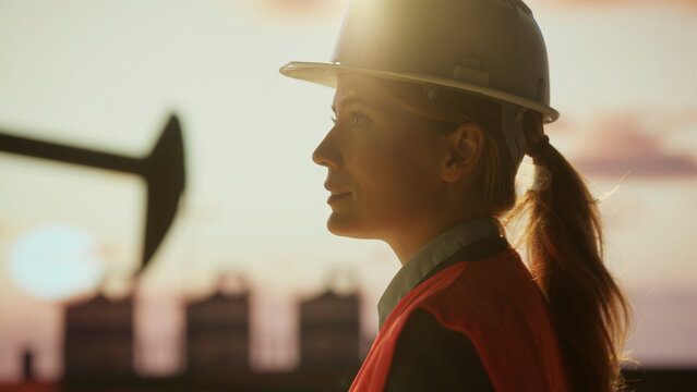 Female engineer wearing hardhat supervising work at oil field at sunset