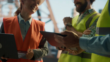 Engineers and contractors discussing project using tablet and laptop at construction site