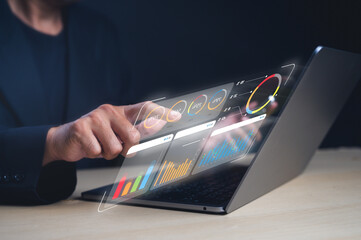 A person interacts with a futuristic transparent touchscreen displaying colorful charts and graphs...