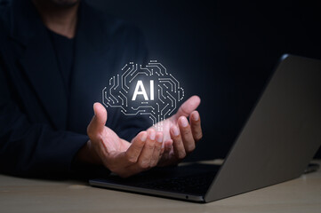 A person holds a glowing AI symbol above their hands next to a laptop, symbolizing artificial intelligence and technology innovation.