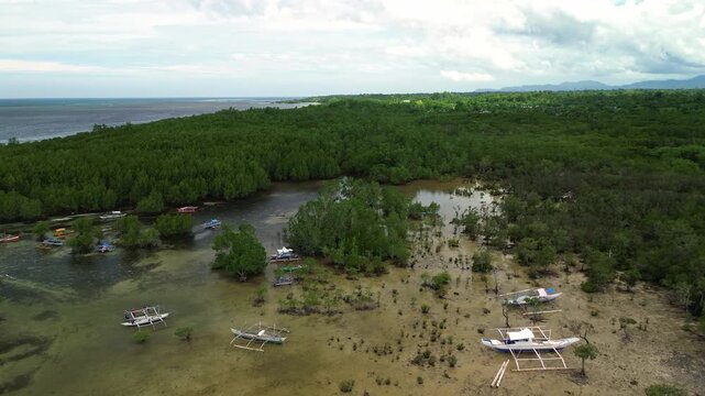 Low-altitude drone glides across Barimbing Beach shallows near San Jose, Puerto Princesa, where outrigger bancas rest beside lush mangrove islets against striped aquamarine Sulu Sea and distant mounta