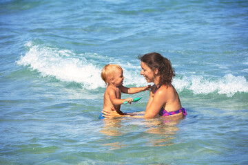 A happy mother bathes her joyful child in the sea