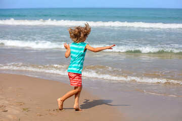Happy playful little boy running on the beach in summer on a sunny day.