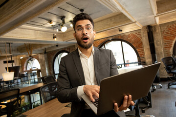 Young man with laptop looking surprised and emotional