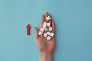 A hand holding sugar cubes with a red arrow pointing upwards, symbolizing an increase in blood sugar