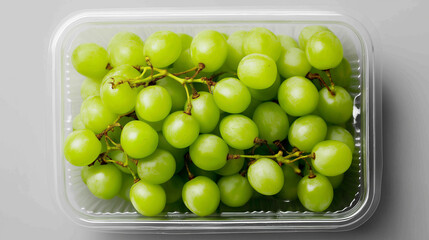 Fresh green grapes with stems packed in a clear plastic container on a neutral background.
