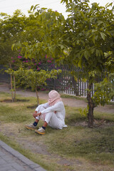 Contemplative person in traditional attire sitting peacefully under a tree in a serene outdoor...