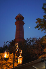 Minaret framed by trees under a blue sky and Moon. Blend of Architecture and Nature representing...