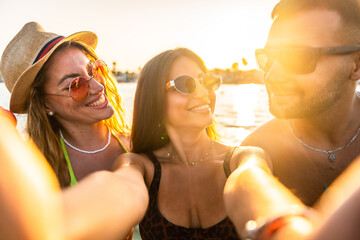 Happy friends taking selfie at beach during sunset