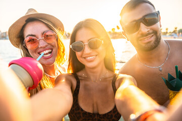 Happy friends taking selfie at beach party during sunset