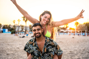 Happy couple having fun on beach at sunset, piggyback ride and victory sign