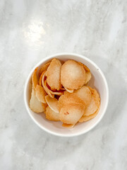 Crispy golden keropok served in a white bowl on marble, a traditional Malaysian snack with irresistible crunch and aroma.
