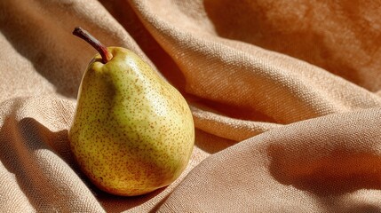 A ripe green pear rests on a soft, beige fabric. The pear has a smooth skin with small speckles and a slender brown stem.
