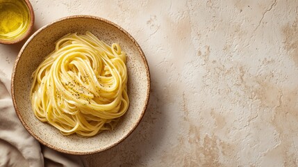 A bowl of spaghetti pasta with olive oil on a textured surface. The dish is simple and elegant, showcasing the pasta's smooth texture and golden color.