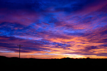 Vibrant Sunset Clouds Over Silhouetted Landscape With Power Line Poles.
