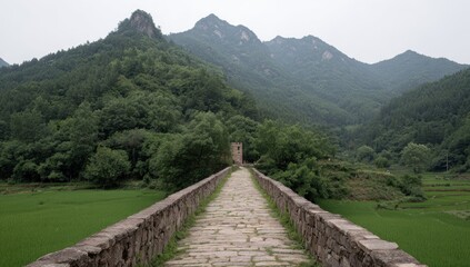 Stone bridge leads toward mountains. Lush greenery covers peaks and valley sides. Rural farmland flanks bridge entrance in a serene, natural scene
