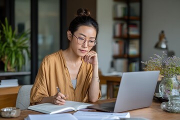 Asian business woman working from home on laptop while taking notes in cozy workspace during the day
