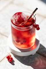 Berry lemonade in a glass with ice spheres with frozen red currant berries
