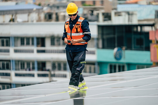 Construction worker inspects solar panels on a rooftop in an urban setting during daytime hours