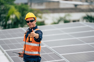 Man on roof gives thumbs up after installing solar panels in urban setting during sunny daytime