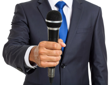 A person in a dark suit and blue tie is holding a microphone forward, suggesting an interview or speech.