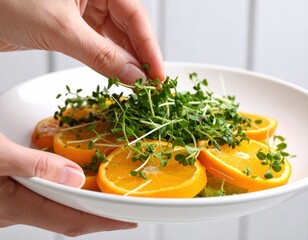 Citrus Harmony Hand Garnishing Orange Slices with Fresh Microgreens in White Bowl.