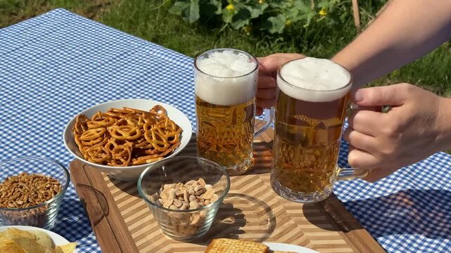 A picnic scene with two hands holding beer mugs, surrounded by pretzels, bread, and snacks, ideal for Oktoberfest celebrations