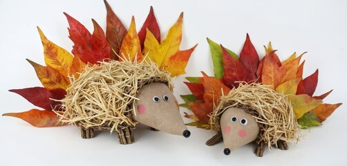 Hedgehog figures crafted from autumn leaves, straw, standing upright against white background. Two charming hedgehogs made with care, attention to detail. One hedgehog long, spiky tail curled around,